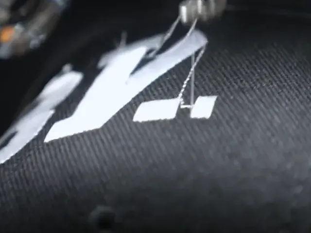 Detail: Logo wird auf dunklen Stoff gestickt